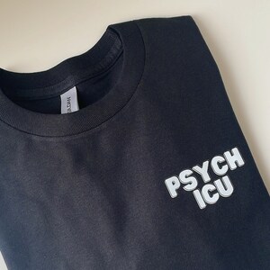 May include: Black t-shirt with white text that reads "PSYCH ICU" in a bold, blocky font.