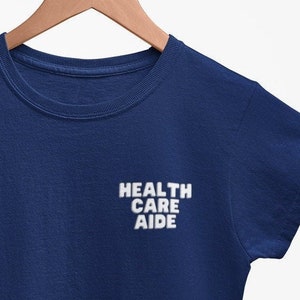 May include: A navy blue t-shirt with the text "HEALTH CARE AIDE" printed in white on the front.