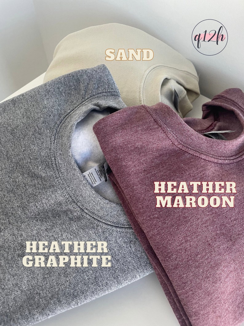 May include: Three folded sweatshirts in different colors: heather graphite, sand, and heather maroon. The sweatshirts are labeled with their respective colors.