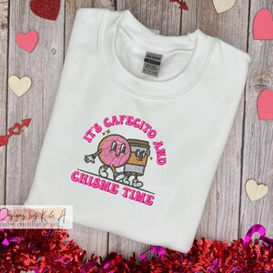 Puede incluir: Sudadera blanca con bordado rosa que dice "It's cafecito and chisme time" con un gr&aacute;fico de donut y taza de caf&eacute;.