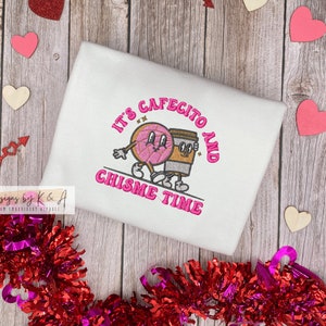 Puede incluir: Sudadera blanca con bordado rosa que dice "It's Cafecito and Chisime Time" con una ilustraci&oacute;n de dibujos animados de una dona y una taza de caf&eacute;.