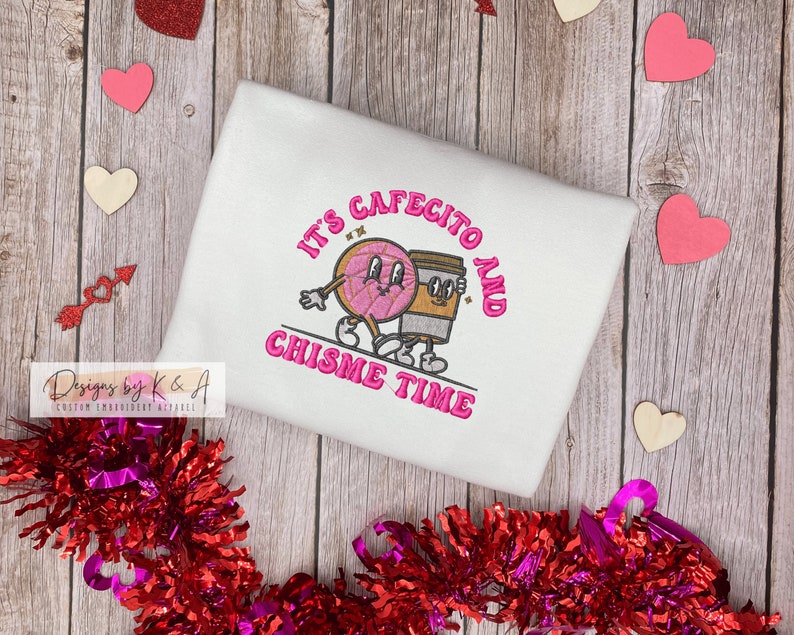 Puede incluir: Sudadera blanca con bordado rosa que dice "It's Cafecito and Chisime Time" con una ilustraci&oacute;n de dibujos animados de una dona y una taza de caf&eacute;.