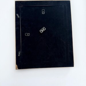 May include: A black picture frame with a gold trim. The frame has four metal hanging hooks on the back.