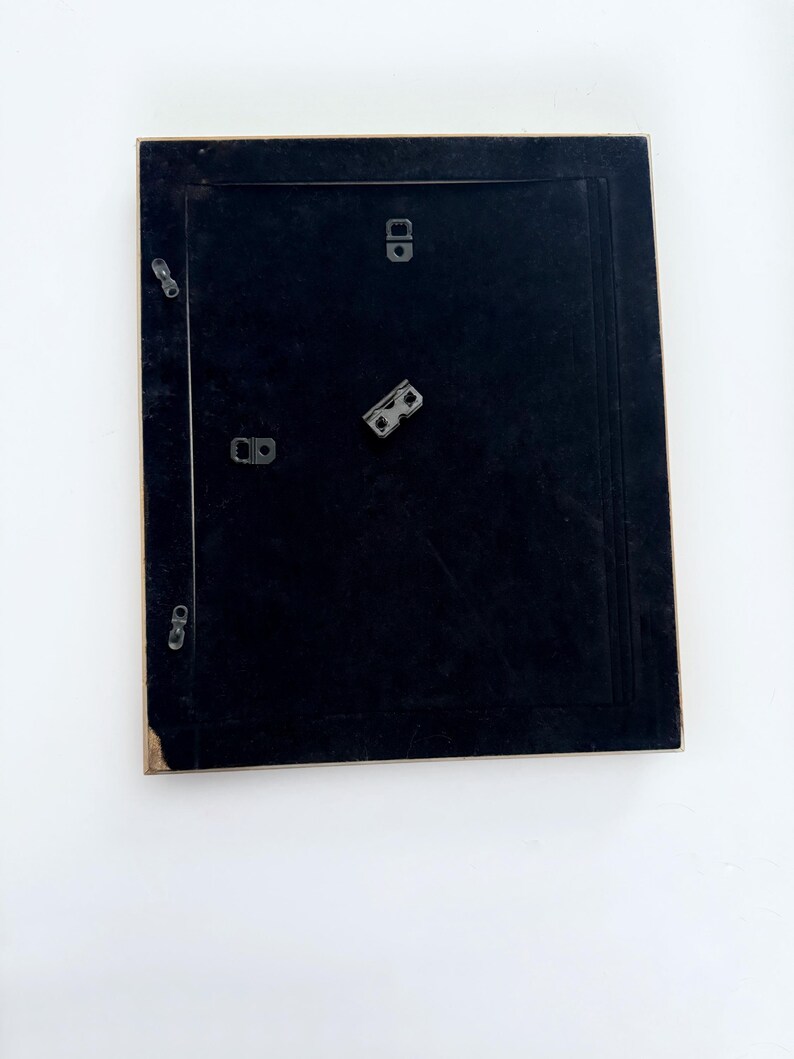 May include: A black picture frame with a gold trim. The frame has four metal hanging hooks on the back.