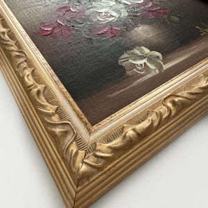 May include: A framed oil painting of a bouquet of white and red roses in a vase. The painting is set against a dark background and has a gold frame with a white inner border.