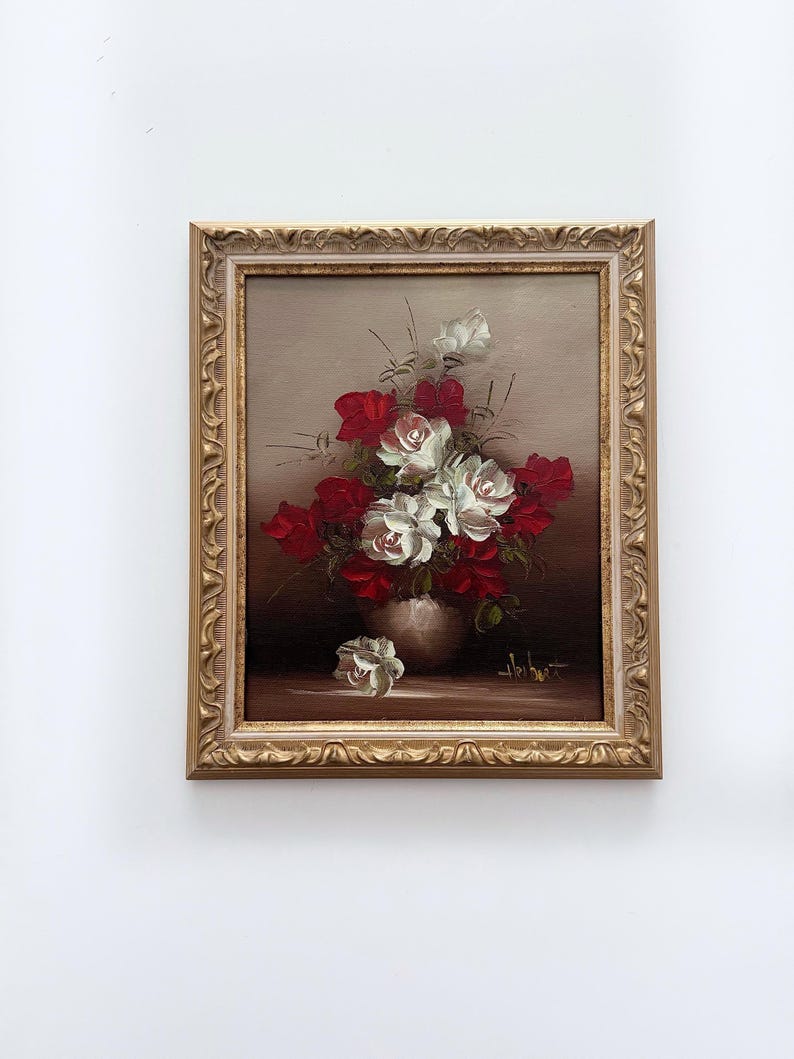 May include: A framed oil painting of a bouquet of red and white roses in a vase. The painting has a brown background and a gold frame.