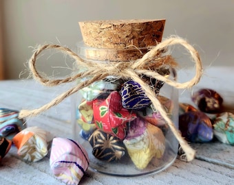 May include: A glass jar with a cork lid filled with colorful origami stars. The jar is tied with twine and has a rustic, handmade aesthetic.