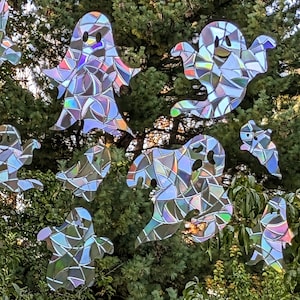 May include: A set of iridescent, holographic ghost cutouts, perfect for Halloween decorations. The ghosts are made of a reflective material that shimmers in the light. They are hanging from a tree branch.