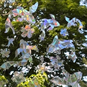 May include: A collection of iridescent window decals featuring multiple koi fish and cherry blossom shapes. Each decal is composed of geometric, stained-glass style segments that reflect a spectrum of colors, creating a shimmering effect.