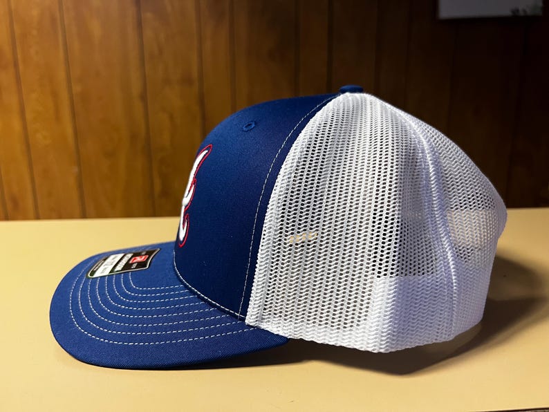 Puede incluir: Una gorra de b&eacute;isbol azul y blanca con un logotipo rojo y blanco. La gorra tiene una parte trasera de malla y una parte delantera s&oacute;lida.