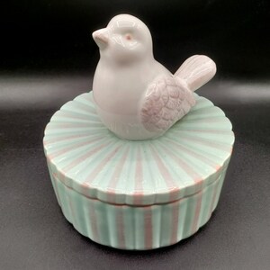 May include: A ceramic trinket box with a white bird lid. The box is decorated with alternating pink and light blue stripes.