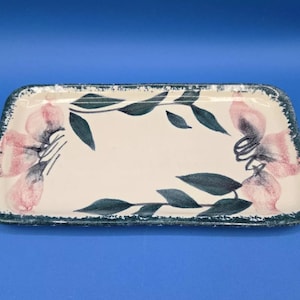 May include: A rectangular ceramic serving tray with a white background and a green and pink floral design. The tray has a green border.
