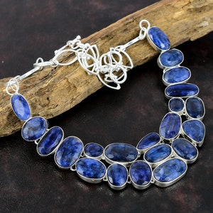 May include: A silver necklace with a double row of oval-shaped blue gemstones. The necklace has a lobster claw clasp.