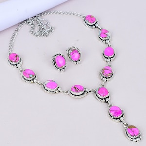 Könnte beinhalten: Ein silberfarbenes Halsketten- und Ohrring-Set. Der Schmuck besteht aus ovalen, leuchtend rosa Steinen mit marmoriertem Aussehen. Die Steine sind in eine dekorative, strukturierte silberfarbene Metalleinfassung gefasst. Die Halskette hat eine Kette und einen Anhänger.