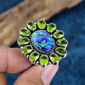 May include: A silver ring with a large oval abalone shell center stone surrounded by 12 smaller oval green peridot stones.