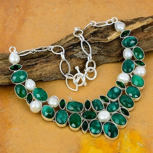 May include: A silver necklace with a green and white gemstone design. The necklace features oval-shaped green gemstones and round white pearls.