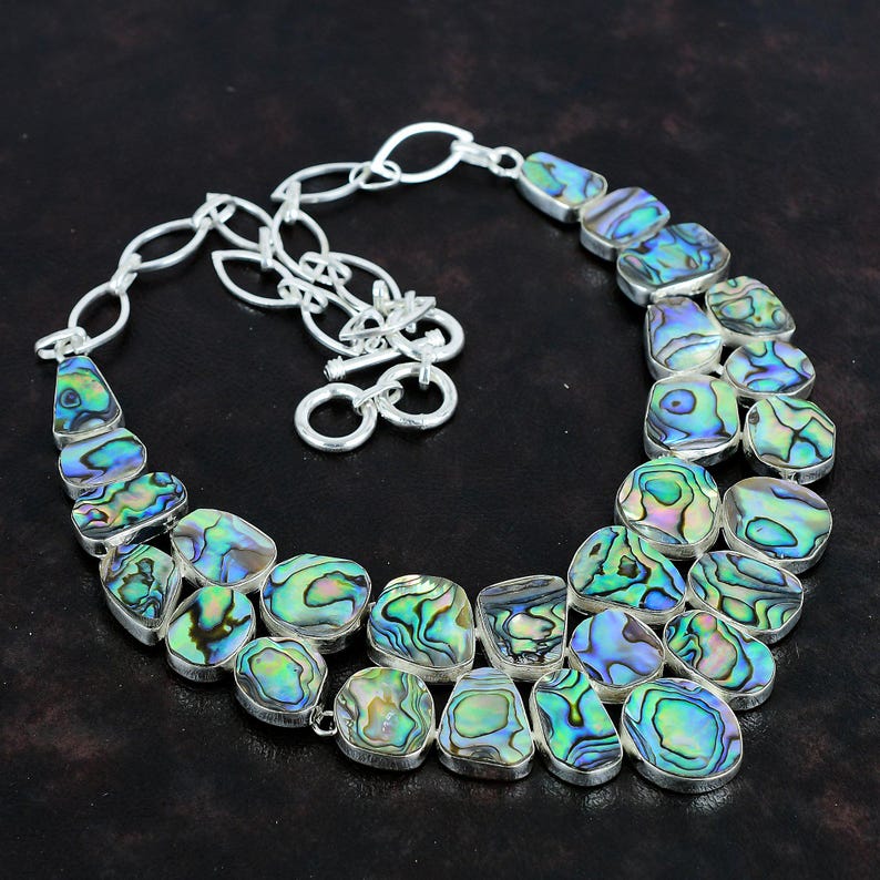May include: A silver chain necklace with a double row of iridescent abalone shell pendants. The necklace has a lobster claw clasp.