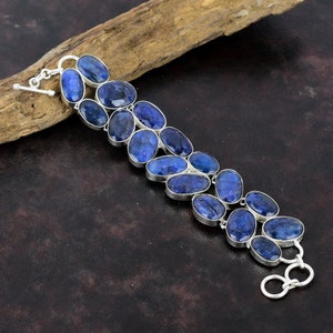 May include: A silver bracelet with a row of oval-shaped blue gemstones. The bracelet has a toggle clasp.