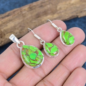 May include: A set of silver earrings and a pendant featuring green turquoise stones. The stones have a marbled pattern with brown veins.