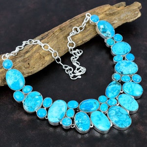 May include: A turquoise and silver necklace with a statement design featuring multiple oval-shaped turquoise stones. The necklace is made with a silver chain and has a lobster clasp closure.