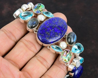 Könnte beinhalten: Ein silbernes Armband mit einem großen ovalen Lapislazuli-Edelstein, umgeben von kleineren blauen Topas-, Abalone- und Perlen-Edelsteinen.