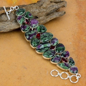 May include: A green and purple gemstone bracelet with red gemstones. The bracelet is made of silver and has a lobster clasp.