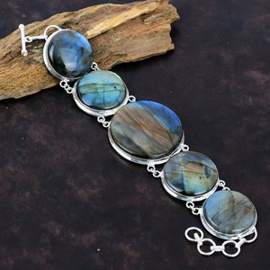 Könnte beinhalten: Ein silbernes Armband mit fünf runden Labradorit-Edelsteinen. Die Steine sind eine Mischung aus Blau, Grün und Braun mit schimmerndem Regenbogenfarben.