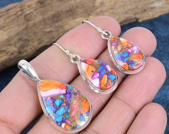 May include: A jewelry set featuring a pendant and matching earrings. The teardrop-shaped pieces have a silver-colored border and are filled with a mosaic of orange, pink, blue, purple, and gold-colored stones. The earrings have a hook closure.
