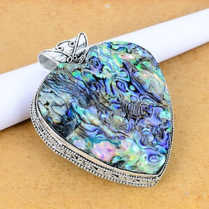 Può includere: Ciondolo a forma di cuore con intarsio di conchiglia di abalone iridescente, con blu, verdi e viola. Il ciondolo è incorniciato in metallo argentato con un bordo ornato e un'ansa decorativa.