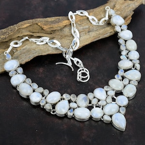 Pode incluir: Um colar de prata com um pingente de pedra da lua branca. O colar é feito de uma corrente com um fecho de lagosta e apresenta um cacho de pedras da lua em forma de lágrima.