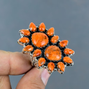May include: A silver ring with a cluster of orange coral stones set in a sunburst design.