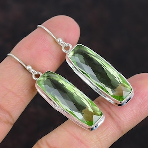 May include: A pair of silver dangle earrings with rectangular green gemstones. The earrings have a simple design and are perfect for everyday wear.