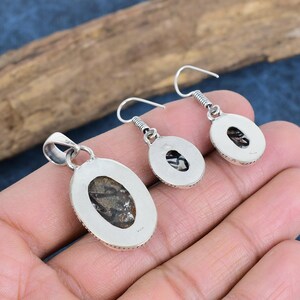 May include: A silver pendant and earrings set with oval-shaped stones. The stones are a dark brown color with a mottled pattern. The pendant has a bail at the top for attaching a chain.