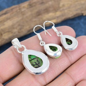 May include: A silver pendant and earrings set featuring a green stone. The pendant and earrings are shaped like teardrops.