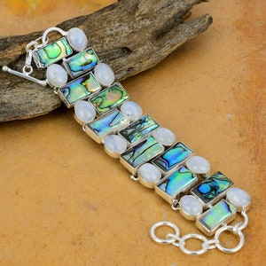 May include: A silver bracelet featuring alternating iridescent abalone shell and white moonstone rectangular beads. The bracelet has a toggle clasp.