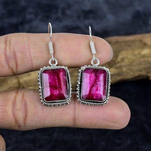 May include: A pair of silver earrings with pink gemstone rectangular drops. The earrings have a delicate, intricate design.