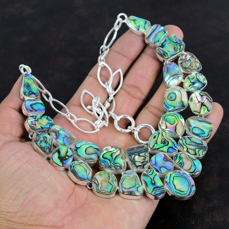 May include: A silver chain necklace featuring a large, multi-coloured abalone shell pendant. The pendant is composed of several individual shell pieces, each with a unique iridescent pattern.