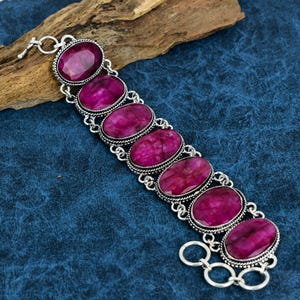 May include: A silver bracelet with seven oval-shaped pink gemstones. The bracelet has a clasp closure.