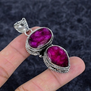 May include: A silver pendant with two large, oval and teardrop-shaped, deep magenta gemstones. The gemstones are set in ornate silver settings with detailed filigree. The pendant has a decorative bail.