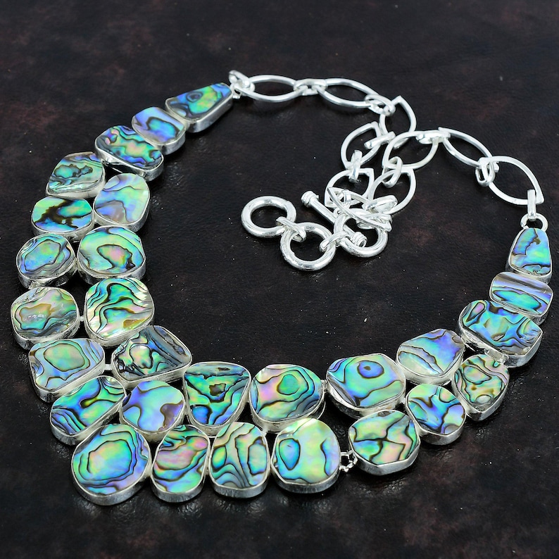 May include: A silver chain necklace with a large abalone shell pendant. The pendant is made up of multiple iridescent green, blue, and purple abalone shell pieces.
