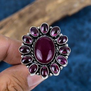 May include: A silver ring with a large oval purple gemstone surrounded by smaller purple gemstones.