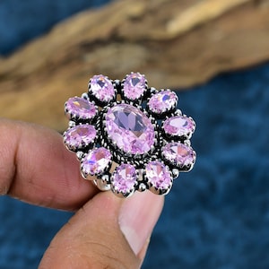 May include: A silver ring featuring a large oval pink gemstone surrounded by smaller pink gemstones.