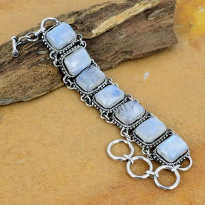 May include: A silver bracelet with a chain link closure and seven rectangular moonstone gemstones. The stones are set in silver bezels with intricate detailing.