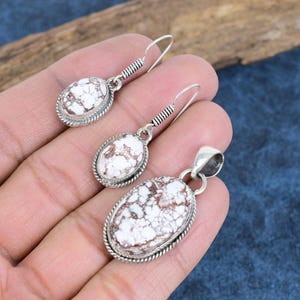 May include: A set of silver earrings and a pendant featuring white and brown oval-shaped stones with a detailed silver border.