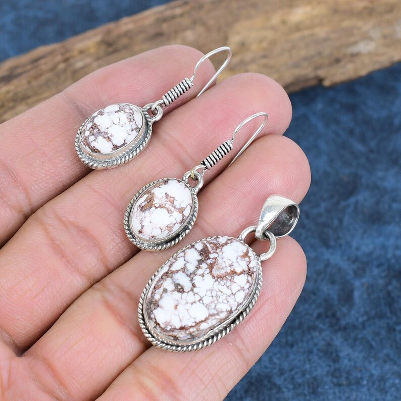 May include: A set of silver earrings and a pendant featuring white and brown oval-shaped stones with a detailed silver border.