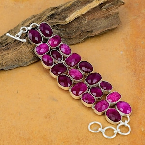 Puede incluir: Una pulsera de plata con una triple fila de piedras ovaladas de color rosa. La pulsera tiene un cierre de langosta y una cadena decorativa.