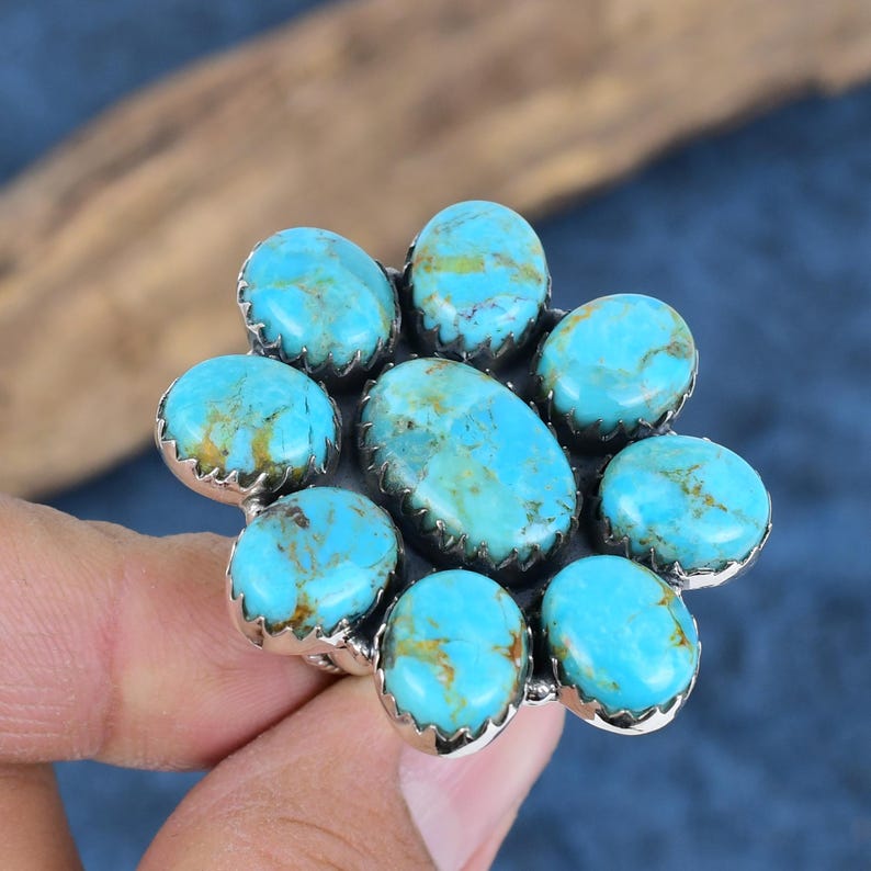 Puede incluir: Un anillo de plata con un grupo de piedras turquesas. Las piedras son ovaladas y redondas, con un color azul brillante y matriz marr&oacute;n. El anillo tiene un dise&ntilde;o floral, con las piedras dispuestas en un patr&oacute;n circular.