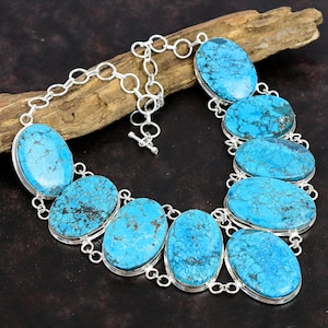 Op de afbeelding: Een turquoise en zilveren statement ketting met ovale turquoise stenen. De ketting is gemaakt van een zilveren ketting met een schuifgesp.