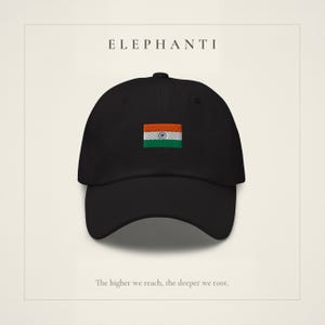 Puede incluir: Una gorra de béisbol negra con la bandera de la India bordada en el centro. El texto ELEPHANTI aparece sobre la gorra, y la frase The higher we reach, the deeper we root. está impresa debajo sobre un fondo claro.