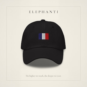 May include: A black baseball cap featuring an embroidered rectangular patch with vertical blue, white, and red stripes on the front. The text ELEPHANTI is printed above the cap, and the text The higher we reach, the deeper we root. is below.
